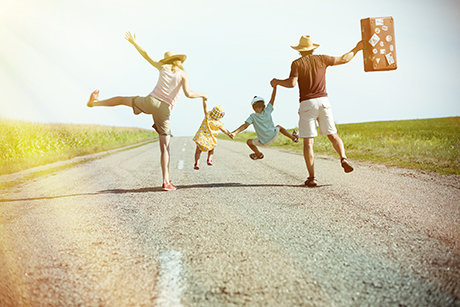 Une famille saute dans les airs, main dans la main : une femme, un homme et deux enfants. L'homme porte une valise de voyage.